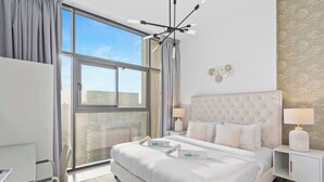 Ein modernes Hotelzimmer mit einem großen Bett, einem Nachttisch, einer Lampe und Blick auf die Stadt durch große Fenster.