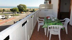 Varanda com mesa e cadeiras, vista para a rua e praia.