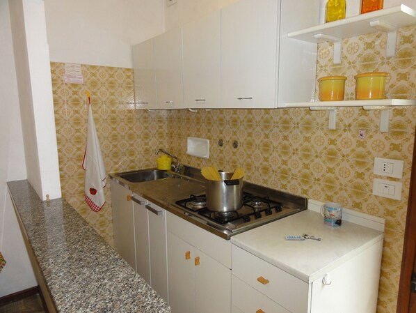 Una cocina compacta con armarios blancos, encimera de granito y estufa a gas.