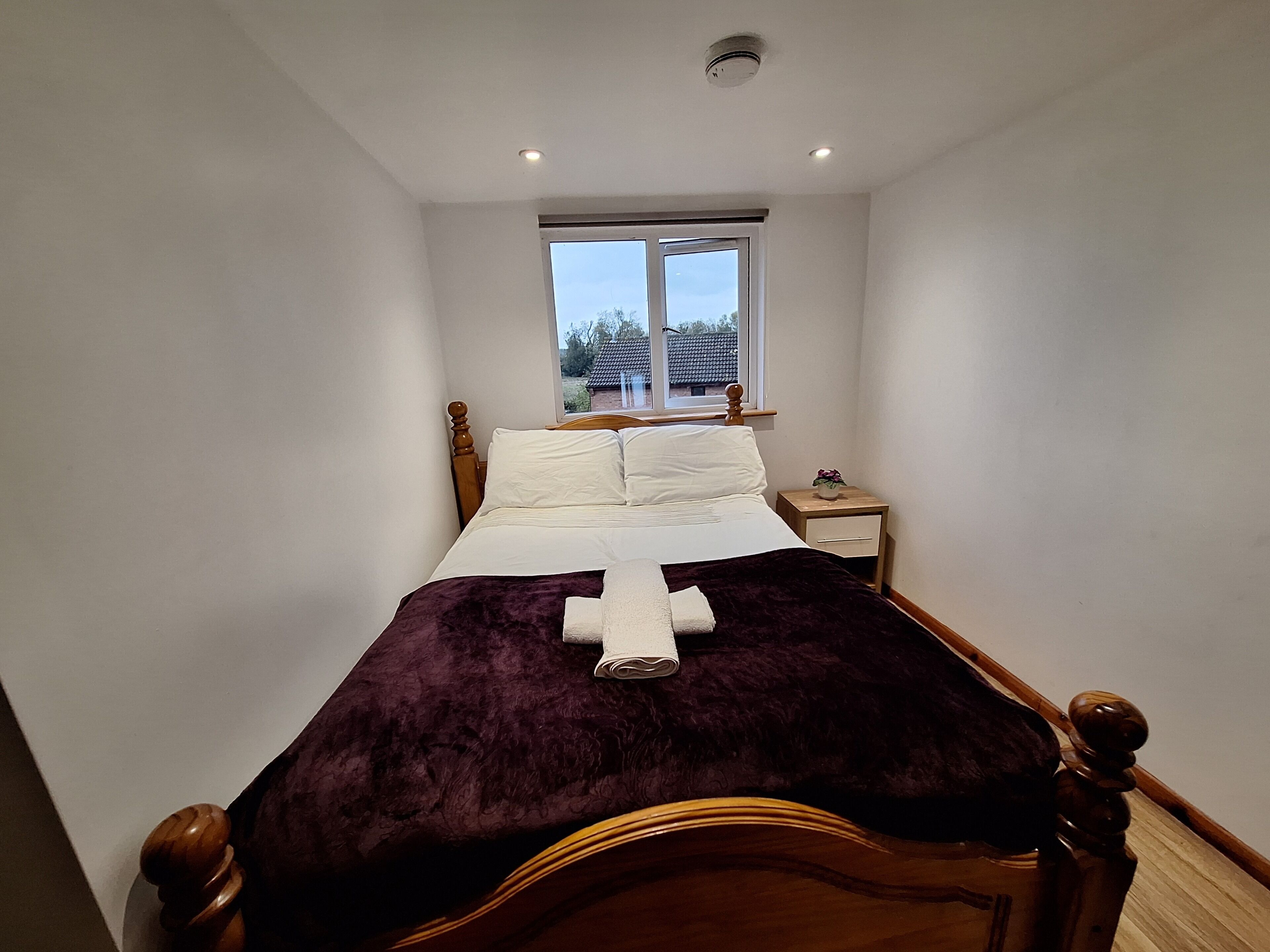 Un dormitorio con cama, mesita de noche, ventana y lámpara en el techo.