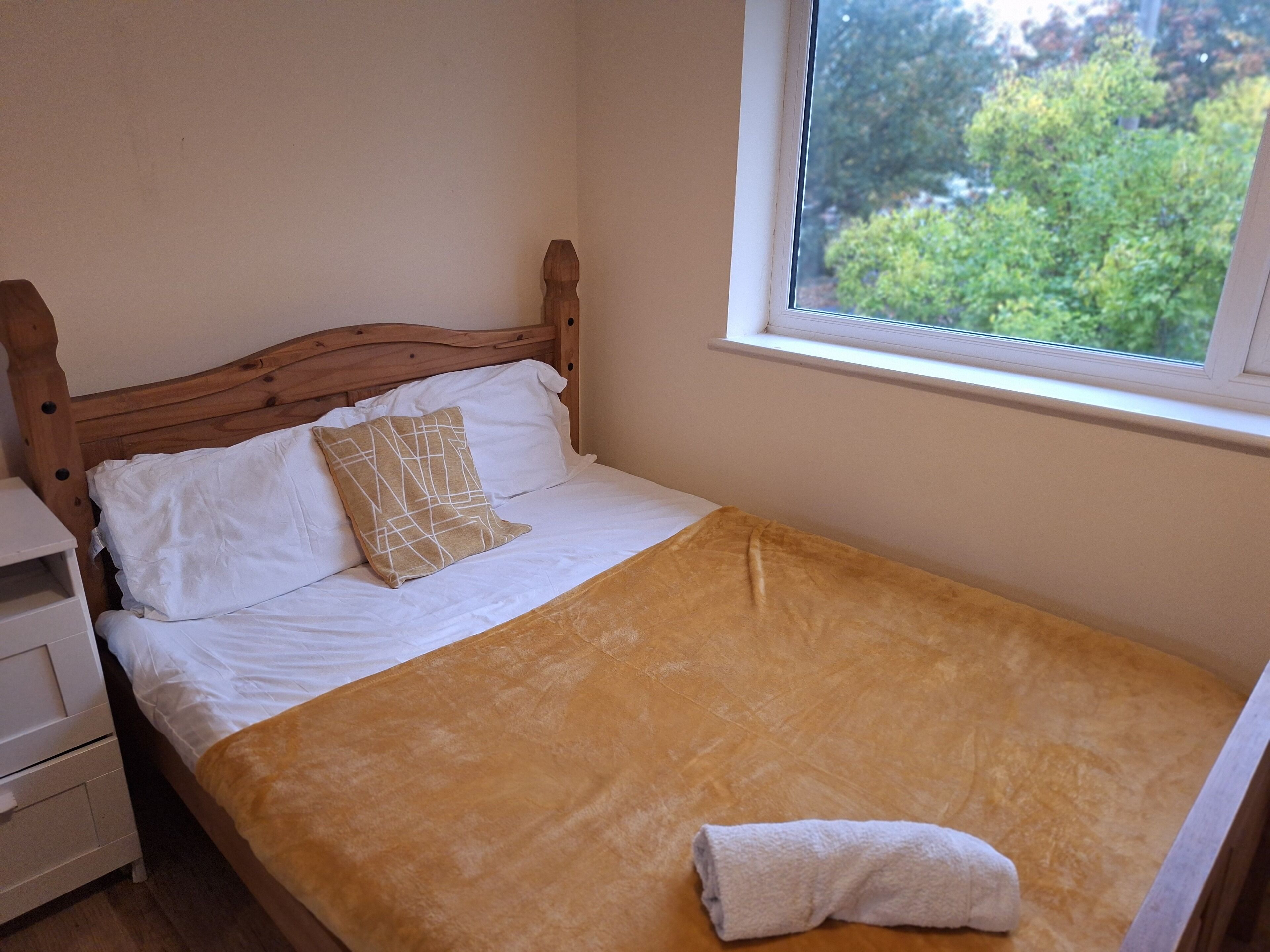 Una cama con cabecera de madera, ropa de cama blanca y una manta marrón.