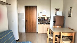 Un ambiente compatto con divano, tavolo da pranzo con sedie, angolo cottura con mobili e una porta che dà su un'altra stanza.