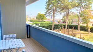Un balcone con tavolo e sedie, con vista su un giardino curato e un’area parcheggio.