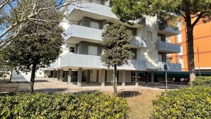 A multi-story building with balconies, surrounded by trees and shrubs. - Flat in seafront condominium with parking (Bibione)