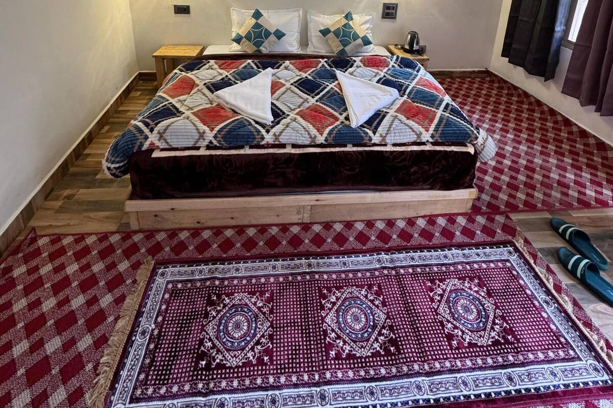 A bedroom with a bed, two wall-mounted light fixtures, a patterned rug, and a window with curtains.
