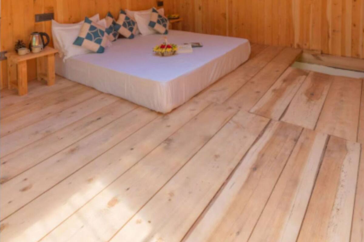 A wooden cabin bedroom with a bed, pillows, a nightstand, and a skylight.