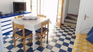 A room with a checkered floor, a table with chairs, a television on a stand, and a door leading outside. - Charming two-storey home (Bibione)