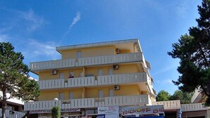 Un edificio de varios pisos con balcones, un letrero y un área verde al frente.