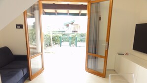 A room with a sliding glass door leading to an outdoor area, a dark blue sofa, a white table, and a mounted TV. - Charming renovated flat (Bibione)