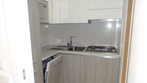 A compact kitchen with a built-in microwave, a sink, and a stove. - Charming renovated flat (Bibione)