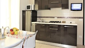 A modern kitchen with dark cabinets, a stainless steel refrigerator, a microwave, and a gas stove.
