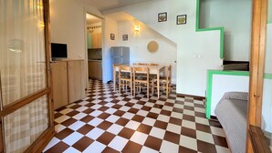 A compact kitchen with a checkered floor, a dining area with a table and chairs, and a small kitchenette. - Bright two-storey flat (Bibione)