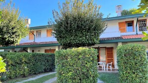 A two-story building with a tiled roof, a covered patio with outdoor furniture, and well-maintained hedges. - Bright two-storey flat (Bibione)