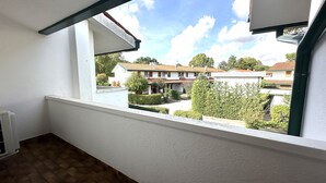 Un balcon donnant sur un quartier résidentiel, avec un sol carrelé et des murs blancs.