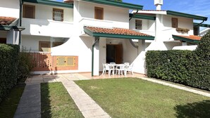 Un bâtiment blanc avec un toit recouvert de tuiles, un patio abrité avec des sièges extérieurs et une pelouse bien entretenue.