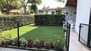 Ein eingezäunter Gartenbereich mit Rasen, Hecke und Blumentöpfen.