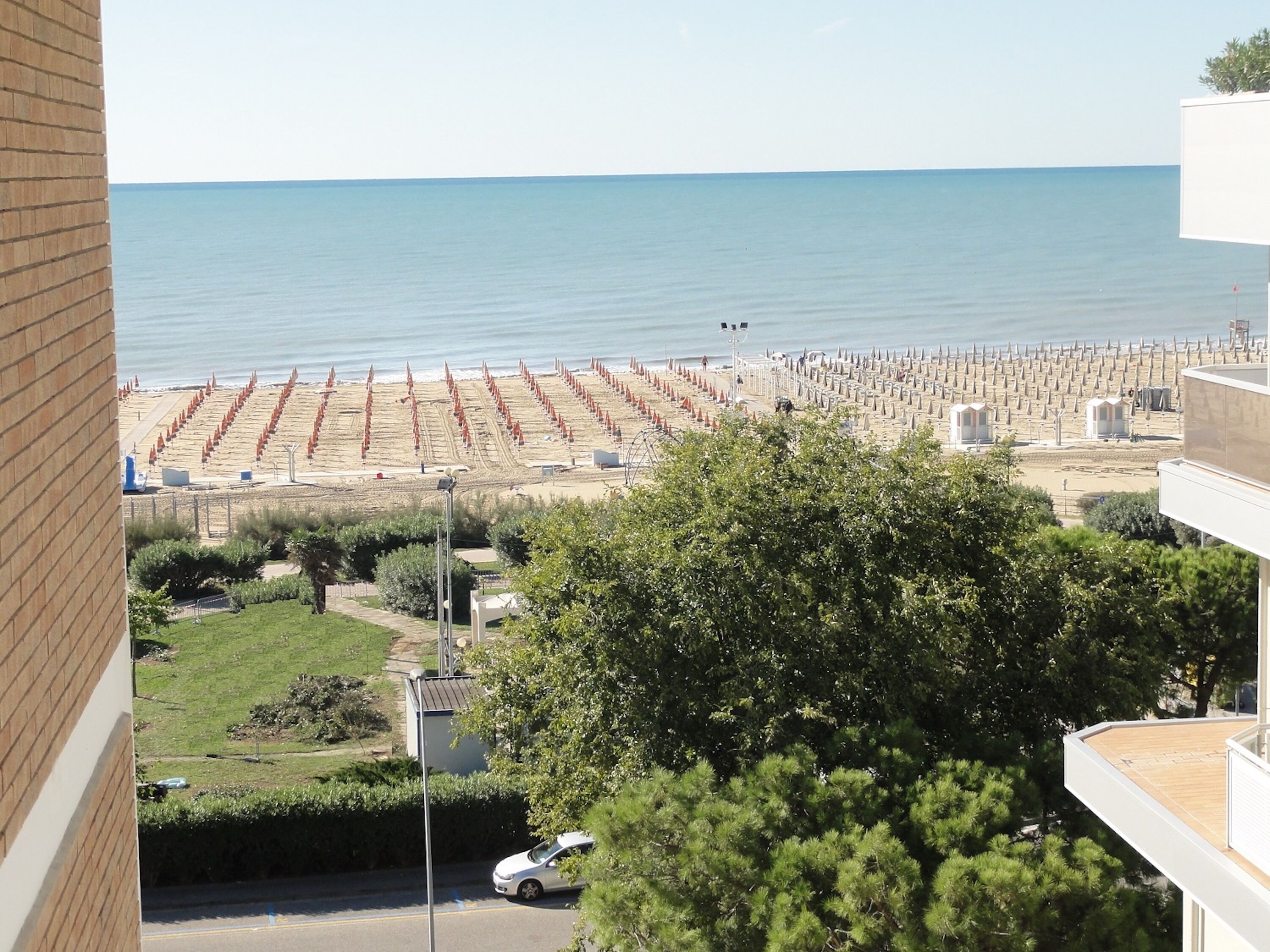 Una playa con hileras de sombrillas y cabañas, cielo despejado y vista al mar.