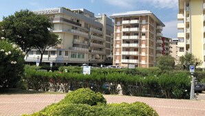 Un immeuble résidentiel à plusieurs étages, doté de balcons, avec un panneau indiquant un espace de stationnement et un arbre au premier plan.