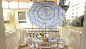Un balcon avec une table ronde, des chaises en plastique blanches et un parasol à rayures.