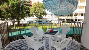 Een balkon met een tafel en stoelen, een vloer met patroon en uitzicht op een zwembad en gebouwen.