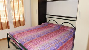 Ein Schlafzimmer mit Bett, Vorhängen, einer Wandleuchte und einem weißen Kleiderschrank.