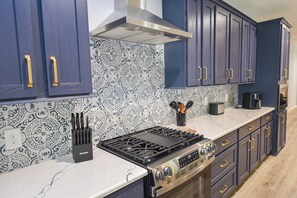 Une cuisine avec des meubles de couleur bleu foncé, une hotte de cuisinière en acier inoxydable, un dosseret à motifs et une cuisinière à gaz.
