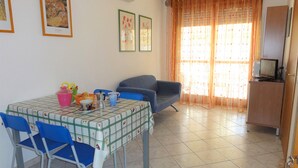 A dining area with a table set for four, blue chairs, a grey sofa, and a television on a wooden cabinet.