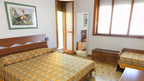 Une chambre à coucher avec un lit en bois, un petit banc en bois, une commode et une fenêtre donnant sur l’extérieur.