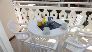 A round white table with four white plastic chairs, a coffee maker, a yellow bottle, and two white cups on a blue placemat. - Bright flat close to the spa (Bibione)