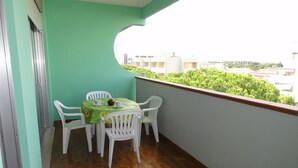A balcony with a table and chairs, a green tablecloth, and a view of buildings and greenery.