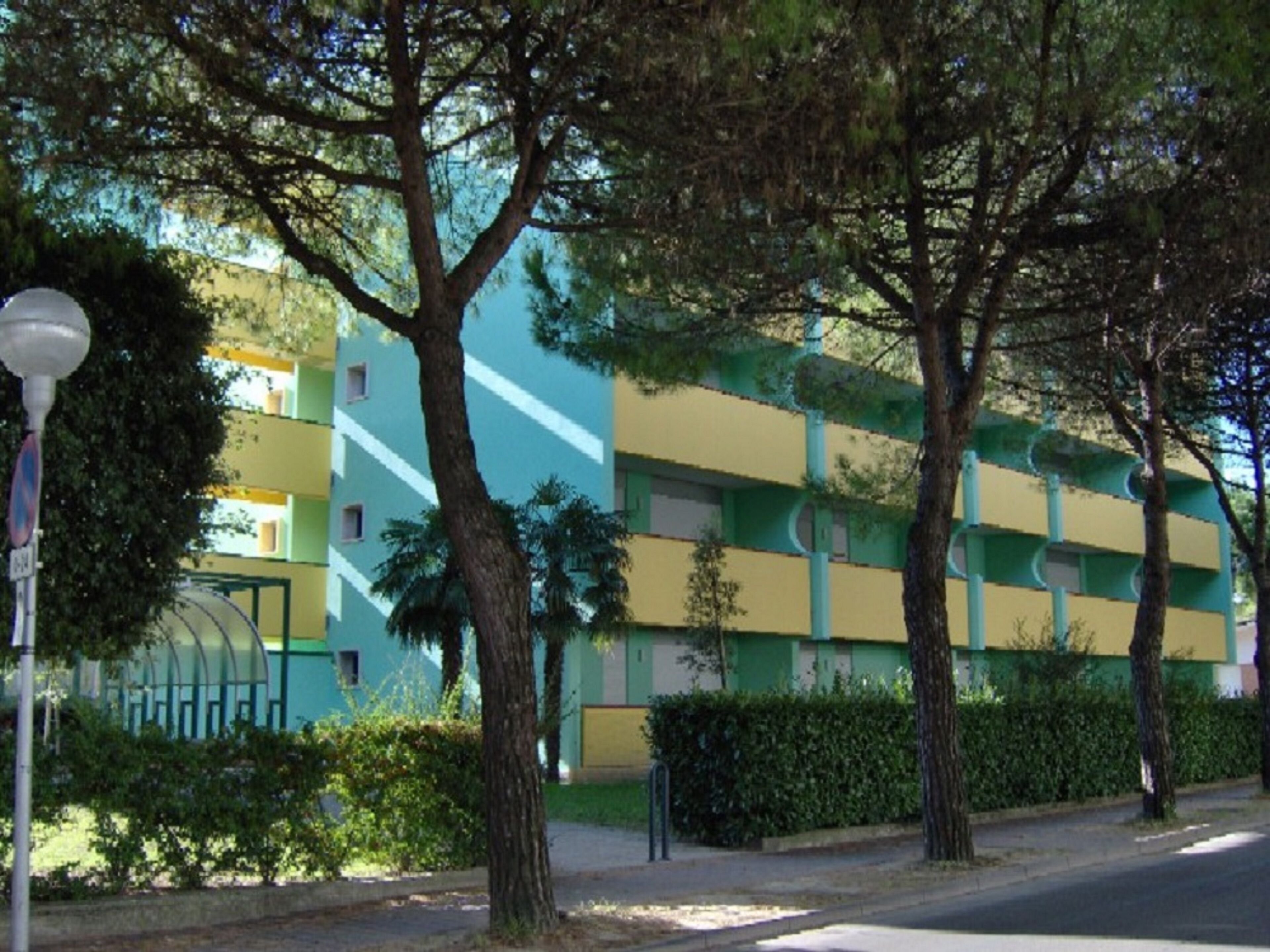 A multi-story building with a green and yellow facade, surrounded by trees and a street lamp.
