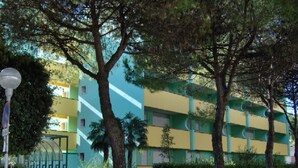 A multi-story building with a green and yellow facade, surrounded by trees and a street lamp.