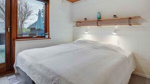 A bedroom with a wooden ceiling, a large bed, a window with an umbrella, and a shelf with decorative items. - 5 Star Holiday Home in Bogense (Bogense)