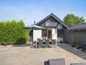 Une maison dotée d’un patio comprenant une table et des chaises, un parasol vert et un barbecue.