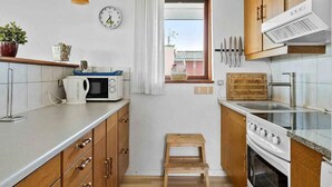 A compact kitchen with wooden cabinets, a microwave, a stove, and a small window with a view. - 5 Star Holiday Home in Bogense (Bogense)