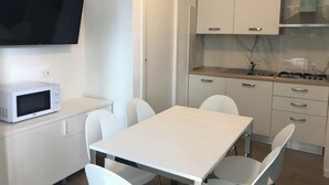 Kompakti keittiö, jossa on valkoiset kaapit, mikroaaltouuni, liesi ja seinälle asennettu televisio, joka on sijoitettu työtason yläpuolelle.