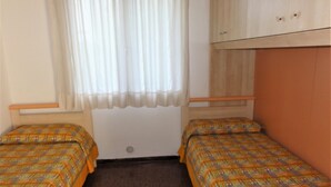 A room with two single beds, a window with sheer curtains, a wooden wardrobe, and a carpeted floor. - Semi-detached villa in a nice area (Bibione)