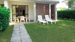 A house with a covered patio, a dining area with a table and chairs, and a well-maintained lawn. - Semi-detached villa in a nice area (Bibione)
