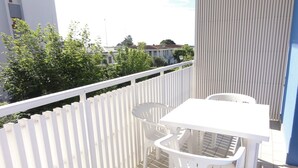 A balcony with white plastic chairs and a table, a white fence, and a view of greenery and buildings in the background. - Bright studio 50mt from the sea (Bibione)