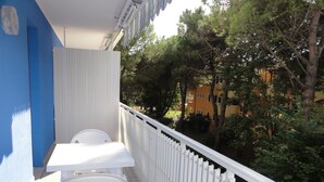 Un balcón con una mesa y sillas blancas, una valla de piquetes blancos y vistas a árboles y edificios.