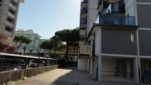 Ein gepflasterter Weg zwischen zwei modernen Mehrfamilienhäusern mit Balkonen, ein klarer Himmel und ein geparktes Auto.