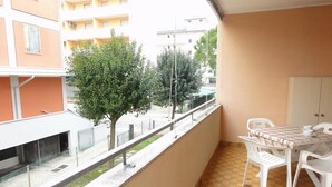 A balcony with a table and chairs, a view of a tree, and a building in the background. - Apartment near the beach in Bibione (Bibione)