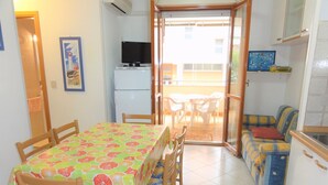 A compact kitchen with a dining area, a refrigerator, a television, and a sofa. - Apartment near the beach in Bibione (Bibione)
