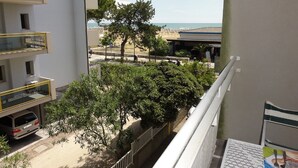 Un balcon donnant sur une plage, un espace de stationnement et un immeuble à plusieurs étages.