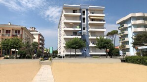 Un immeuble résidentiel à plusieurs étages, doté de balcons, d’une allée pavée et entouré de verdure.