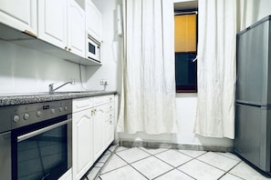 Una cocina con armarios blancos, horno empotrado, microondas y refrigerador de acero inoxidable.