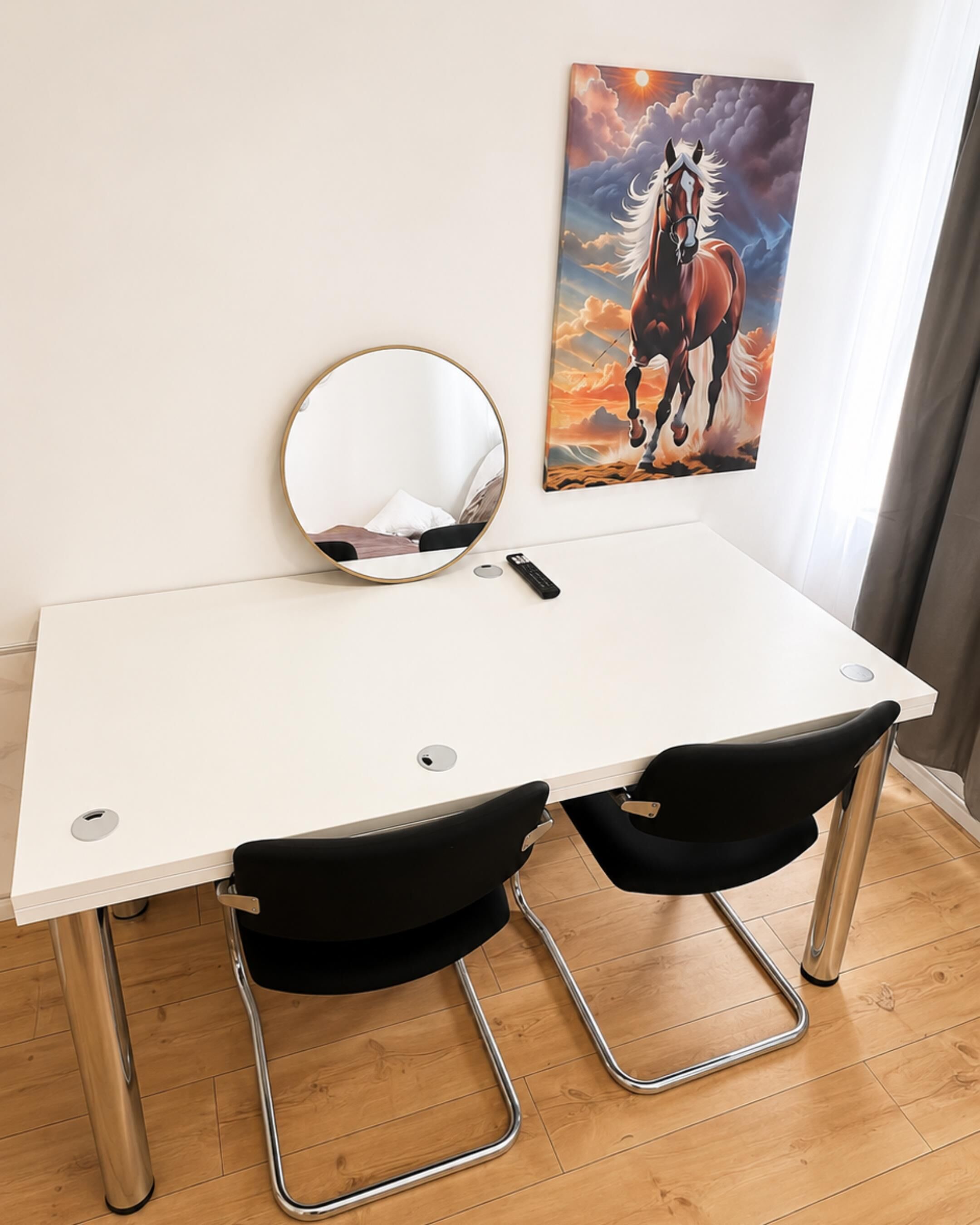 A white desk with two black chairs, a round mirror, and a painting of a horse.