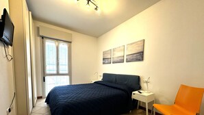 A bedroom with a bed, a chair, a nightstand, a TV, and artwork on the wall. - Bibione apartment with pool and solarium access (Bibione)