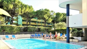 A swimming pool with lounge chairs and a building in the background. - Bibione apartment with pool and solarium access (Bibione)