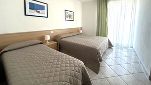 Habitación de hotel con dos camas, un cabecero, una mesita de noche con lámpara y dos cuadros enmarcados en la pared.